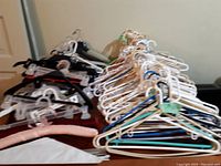 Pile of assorted plastic, wooden, and padded clothes hangers stacked on top of each other