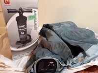 Coleman electric air pump on top of deflated gray air bed with box of Bestway Air Hammer hand pump visible