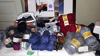 Overview of the lot showing the sewing machine on its box with the iron in front and a large assortment of knitting wool skeins spread around.