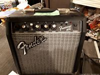 Photo of Fender Frontman 10G guitar amplifier showing front grille, Fender logo, control knobs, input jacks, and power switch.