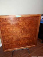 Bottom side of wooden folding game table shows wood flat surface and legs folded out for support.