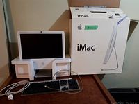 Front view of the iMac 17-inch with wired keyboard and original packaging box on a wooden table.