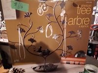 Photo showing metal jewelry tree with several jewelry items hanging, including earrings and necklaces, dark metal color with leaf shaped branches.