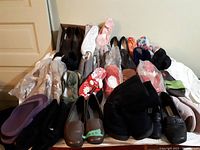 Wide angle showing 22 pairs of women's shoes in various styles and colors arranged on floor and in box, mostly wrapped in plastic, sizes 7 and 9