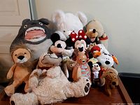Photo showing a collection of 14 assorted plush toys including Totoro, Mickey and Minnie Mouse, lion, white bear, various dogs, and other animals.
