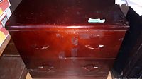Photo of the front of a two-drawer wooden dresser with dark reddish-brown finish showing tape residue on the front and chip marks on top.