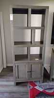 Full view of the grey composite wood bookcase showing six open shelves and double doors at the bottom for closed storage.