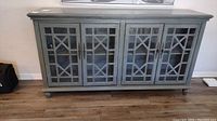 Front view of gray composite buffet with four glass doors and decorative wooden framing.