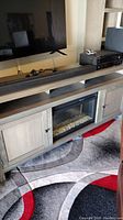 Front view of the cabinet with electric fireplace insert; TV mount or TV on top visible, with soundbar and receiver on cabinet top (not included).
