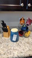 Faberware cutlery set with wooden block, blue ceramic canister, six colorful coffee mugs on metal stand