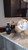 Full view of all items including the globe, two vases, metal sculpture, and wooden box on granite counter