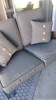 Close view of dark gray cushions and pillows with button details on the outdoor glider seat and backrest.