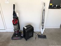 Photo showing Hoover vacuum cleaner, black electric paper shredder, and white Shark floor steamer mop angled upright.