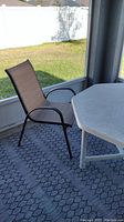 Single outdoor chair positioned next to white plastic outdoor table on grey patterned outdoor rug in screened porch area.
