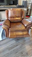 Front view of brown faux leather recliner rocker chair with footrest extended, showing padded back and arm cushions.