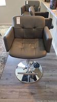 Front view of an adjustable bar stool with charcoal gray faux leather and metallic base on wood flooring.