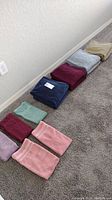 Towels laid out in a row showing various colors including beige, light blue, navy blue, maroon, and green with pink and purple towels in foreground