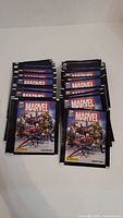 50 unopened Marvel sticker packs arranged in two stacks showing front packaging artwork with multiple superheroes