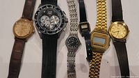Six watches laid out in a row showing a variety of styles and bands including leather and metal.