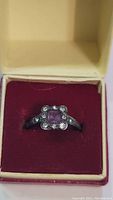Front view of antique silver ring featuring a square purple stone surrounded by clear stones, placed inside a red velvet ring box.