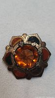 Close-up front view of the antique brooch showing amber-colored glass centerpiece and multi-colored enamel in metal frame.