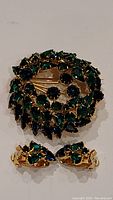 Photo showing round brooch with green and blue rhinestones and matching pair of clip-on earrings laid flat on a white surface