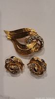 Photo showing the Coro costume jewelry set including a gold tone brooch and matching clip-on earrings with rhinestone detailing.