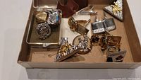 Box containing various cufflinks and a thimble, showing a range of designs and metal finishes including western cowboy boot motifs.