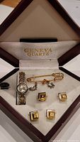 Full view of Geneva Quartz watch set including wristwatch, tie clip with charm, and four cufflinks inside branded box.