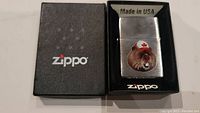 Front view of Zippo lighter in original black box showing the beaver with maple leaf hat design, marked Made in USA.