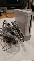 Nintendo Wii console in vertical stand next to a bundle of audio/video and power cables with sensor bar on top.