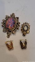Photo showing all four items: large ornate pendant with iridescent center, smaller pendant with white stone and clear stones, butterfly earrings pair