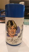 Side of thermos showing caricature portrait of Wayne Gretzky with printed signature and part of hockey scene graphic.