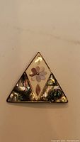 Front view of triangular silver brooch with mother of pearl inlay and abalone shell sections, flower and leaf motifs visible.
