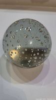 Top view of the solid clear glass spherical paperweight showing numerous small air bubbles inside.
