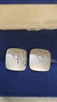 Front view of square sterling silver cufflinks showing engraved floral design on a matte finish surface.