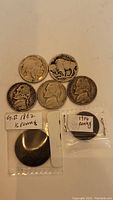 All five coins arranged on a white surface, two Buffalo nickels showing front and back, 1919 penny, 1862 half penny labeled in a plastic sleeve, and an additional silver coin.