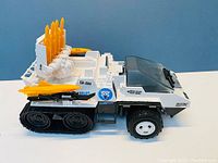 Right side view of GI Joe Snowcat showing tracked rear wheels, yellow missiles on rear rack, side rockets, clear windshield, and decals.
