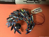 Front photo of antique Sherman brooch showing blue marquise and round rhinestones arranged in a curve with a $1.95 price tag attached.