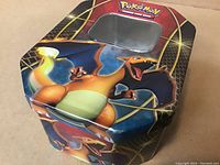 Metal tin featuring vibrant Charizard artwork with a windowed lid, shown from an angle.