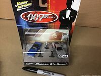 Front view of sealed Johnny Lightning 40th Anniversary James Bond diecast box set with two car models and three character figurines, placed in packaging with branded card backing and graphics.