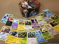 Photo of 18 rare Pokémon cards spread in front of a Pokémon collectible tin showing various cards including Mewtwo, Rayquaza, and Whimsicott.