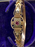 Close-up of front panel showing central faceted red gemstone in starburst setting, flanked by two white stones in star motifs, and surrounding bead and wire filigree