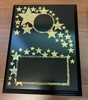 Front view of the award plaque showing gold holographic star decorations and rectangular text area