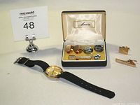 Wide view of the lot showing the Birks watch without strap, and the boxed Anson cufflinks and tie clips with two gold-tone tie clips placed beside the box.