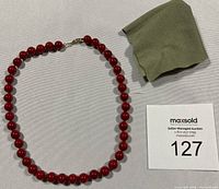 Full view of necklace laid flat with coral beads and decorative clasp, alongside a cleaning cloth and auction lot number.