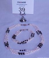 Full set of freshwater pearl necklace and matching bracelet with black stone accents displayed on white surface with MaxSold auction marker.