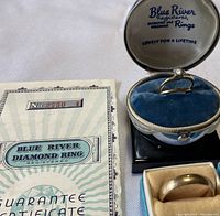 Engagement ring displayed in Blue River white oval box with velvet interior alongside guarantee certificate.