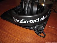 Close-up of Audio-Technica name logo on leather headband of headphones with attached drawstring pouch on wooden surface.