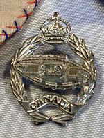 Close-up photo of the WWII Canadian Tank Corps Regiment Cap Badge showing detailed tank, laurel wreath, crown, and banner reading 'CANADA'.